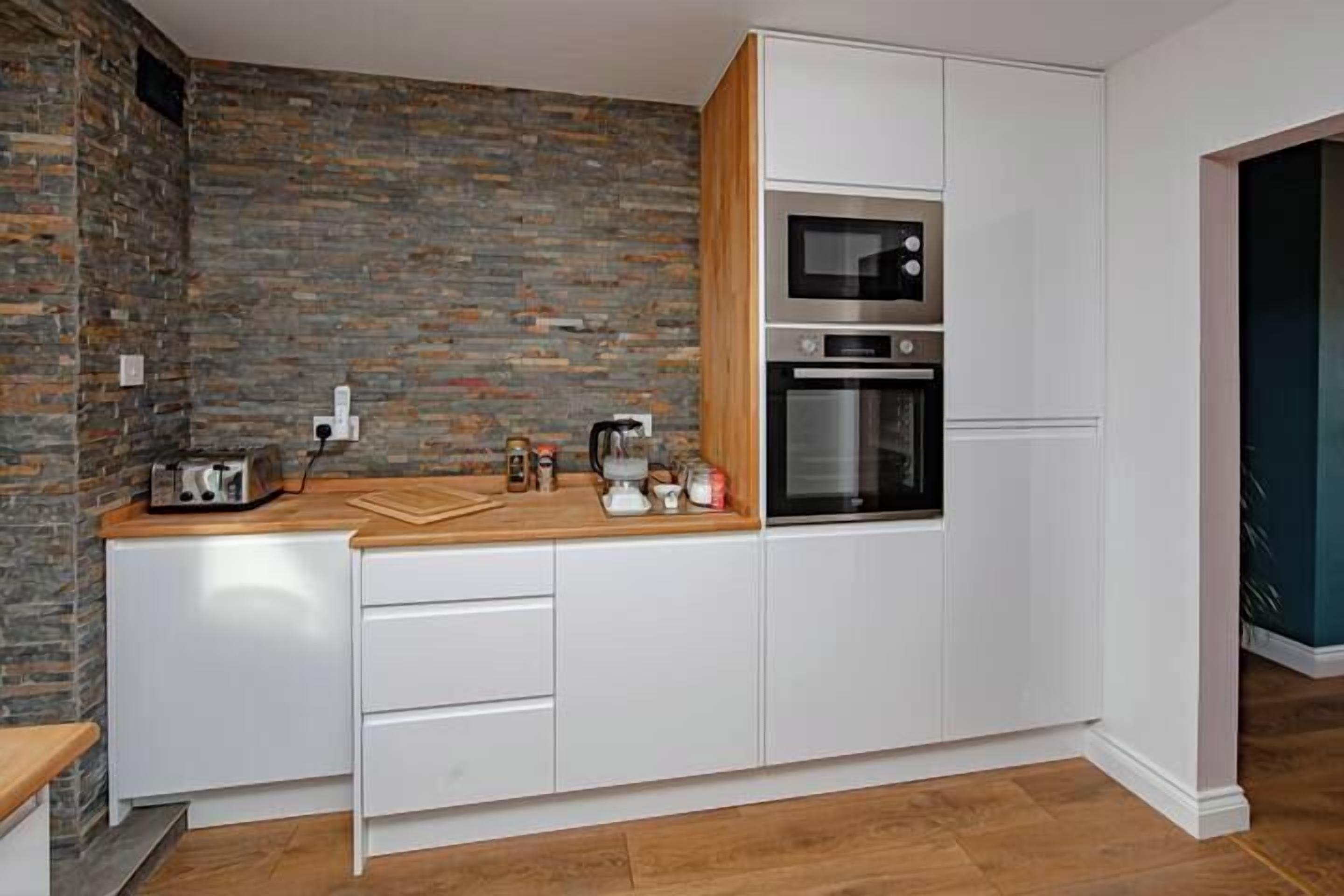 Una cocina compacta con muebles blancos, una pared de ladrillo y un microondas.