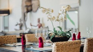 A dining table set with white orchids, clear wine glasses, and red napkins. - Ivory Pool Villa in Nai Harn (Phuket)