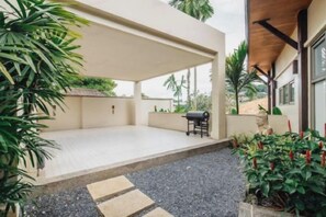 Un espace extérieur couvert, aménagé en patio, avec un barbecue, des sièges et des plantes en pot.