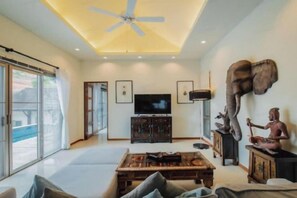 Un salon spacieux doté d’un ventilateur de plafond, d’un téléviseur à écran plat et d’une grande statue.