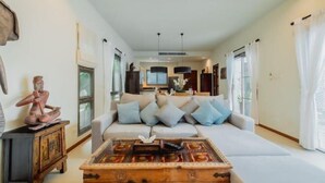 A modern living room with a sofa, coffee table, and artwork. - Ivory Pool Villa in Nai Harn (Phuket)