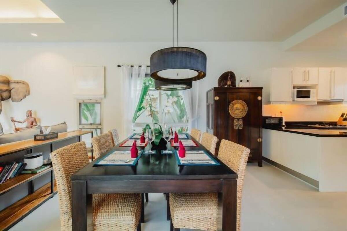 A dining area with a dark wooden table, wicker chairs, and a modern pendant light.