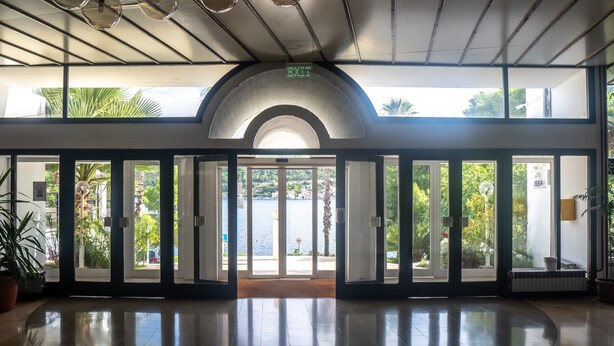 Un hall d’hôtel doté d’une entrée en verre, d’un ventilateur de plafond et offrant une vue sur une étendue d’eau.