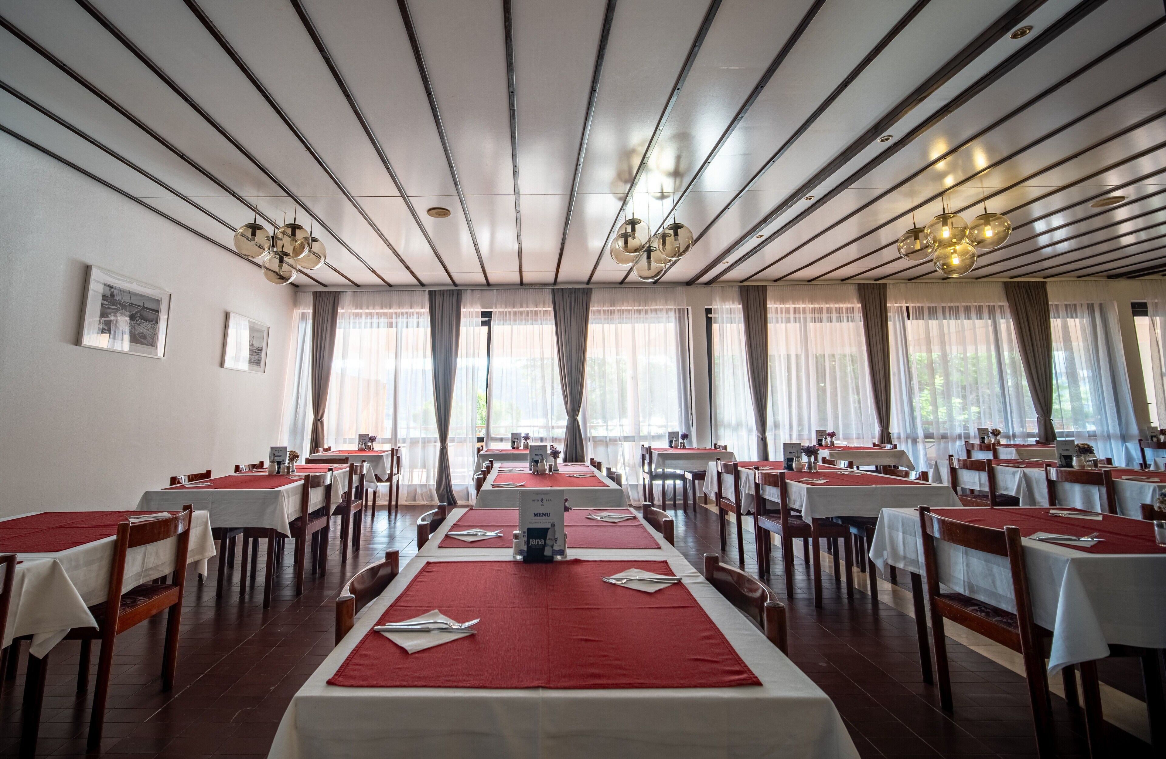 A restaurant with a long table layout, red tablecloths, and a menu sign.