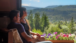 Una pareja sentada junto a una ventana con vistas panorámicas a colinas y árboles.