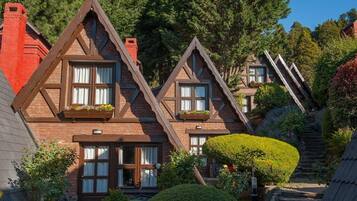Een chalet in traditionele stijl, met steil schuin aflopende daken, dakkapellen en een verzorgde tuin met een haag en een boom.