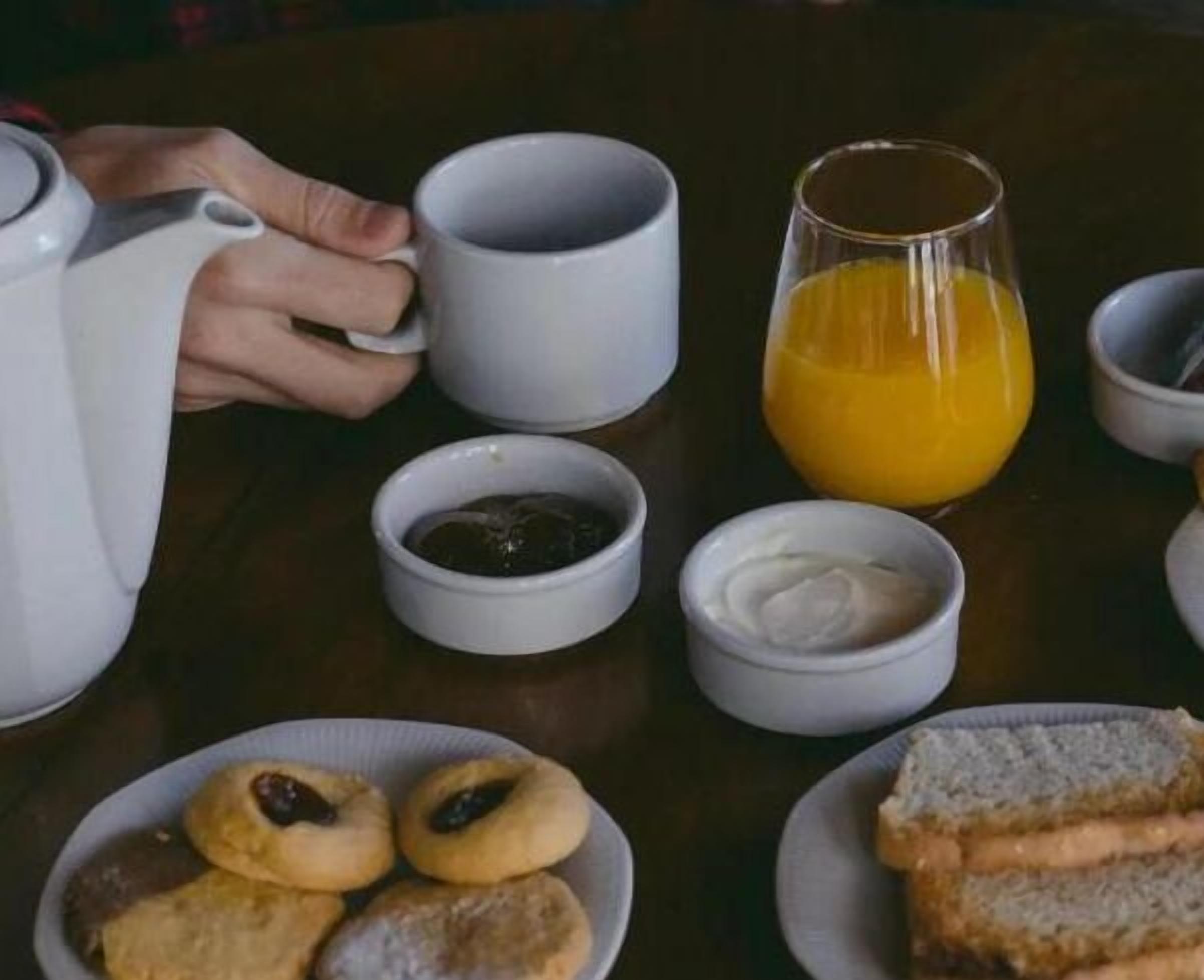 A breakfast table with a teapot, cups, a glass of orange juice, and plates with pastries and toast.