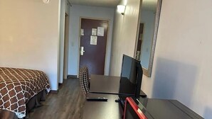 Une chambre d’hôtel avec un lit, un bureau équipé d’un ordinateur et d’un four à micro-ondes, et une porte dotée d’un miroir.