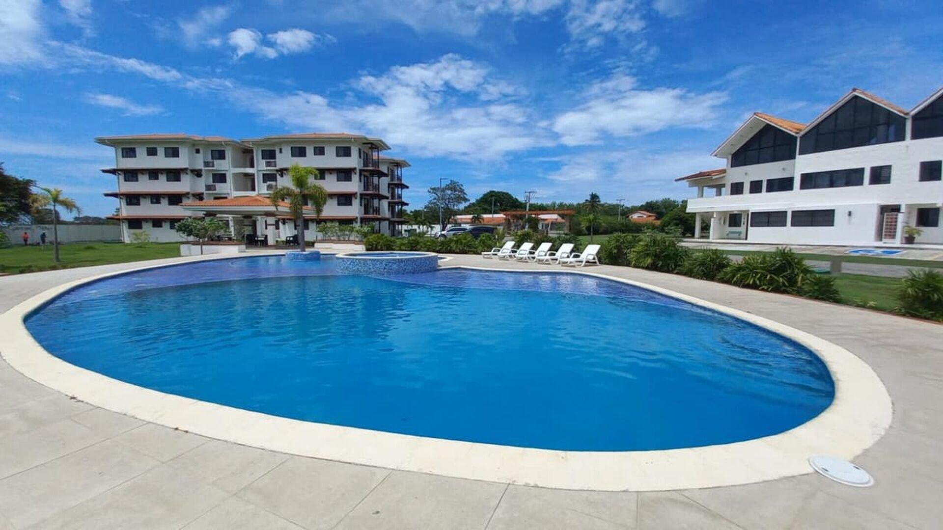 A swimming pool with lounge chairs, surrounded by buildings with a flat roof and multiple floors.
