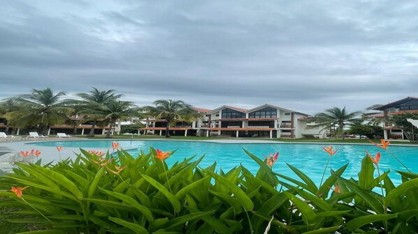 A resort with a swimming pool, palm trees, and a cloudy sky.