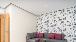 Een moderne woonkamer met een grijze bank, rode kussens en een behang met patroon.