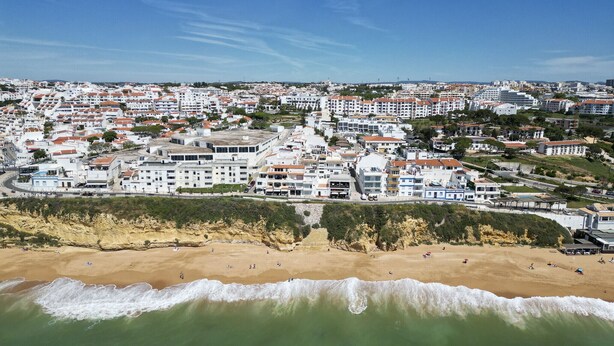 A coastal town with a beach, white buildings, and a clear sky.