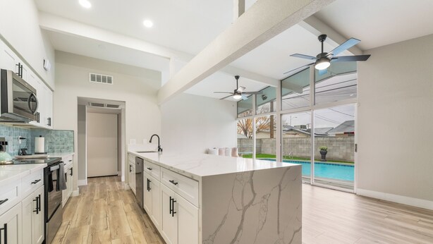 Una cucina moderna con isola in marmo, pavimento in legno e vista su una piscina attraverso ampie finestre.