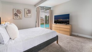 Camera da letto con un letto, una TV, vista su una piscina e opere d'arte appese al muro.