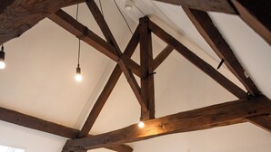 Ein Schlafzimmer mit schrägverdeckter Decke, Holzbalken, einem Bett mit weißen Leinen, Nachttischlampen und einem kleinen weißen Stuhl.