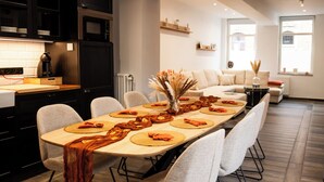 Eine moderne Küche mit dunklen Schränken, ein Essbereich mit einem langen Tisch für sechs Personen und ein Wohnbereich mit einer Couch und einem Couchtisch.