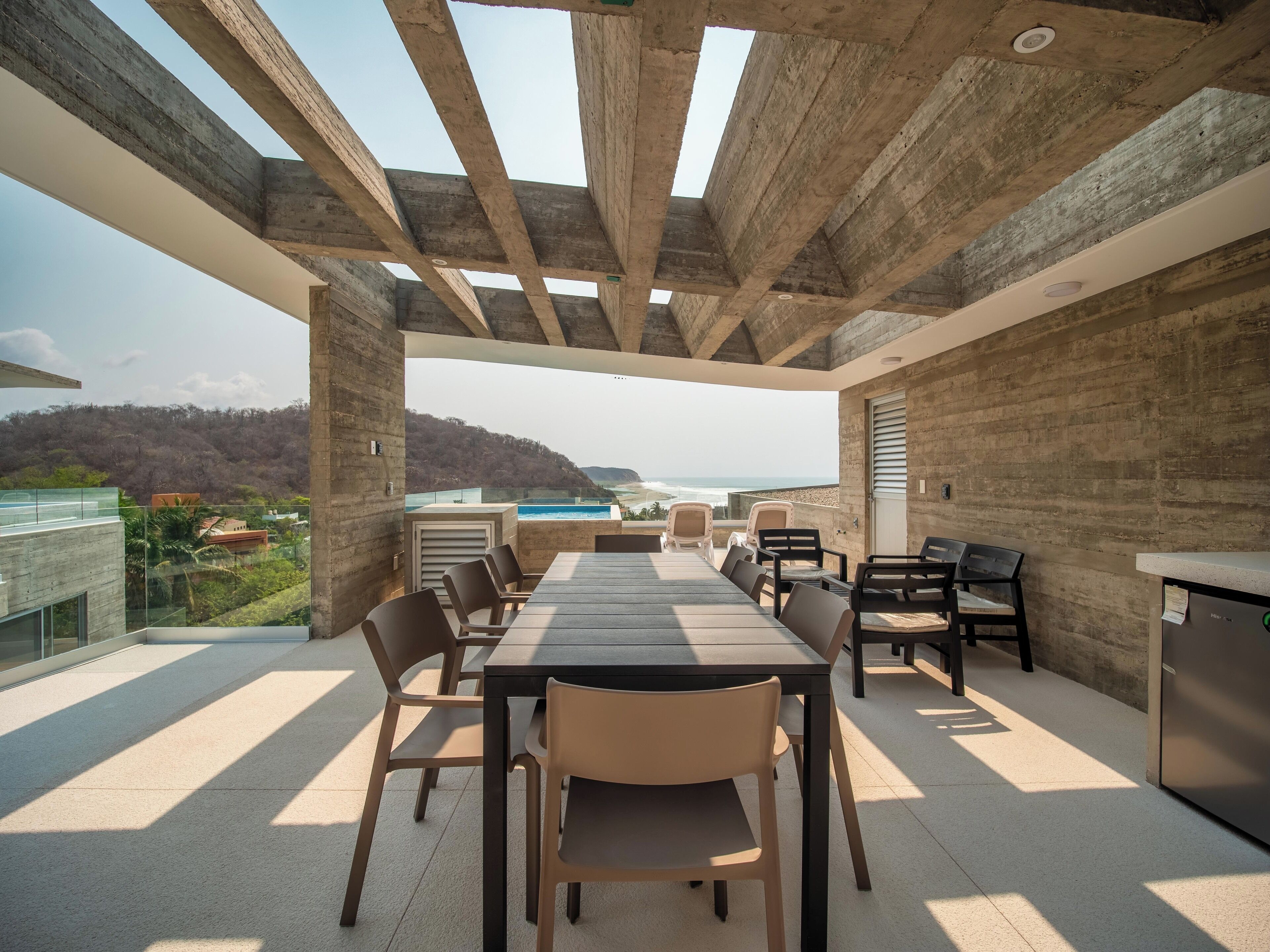 A covered outdoor dining area with a view of the ocean and hills.