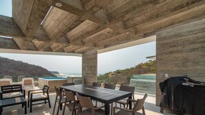 An outdoor patio with a table and chairs, a grill, and a view of the ocean.