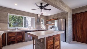 A modern kitchen with a central island, wooden cabinets, a built-in oven, and a large window.