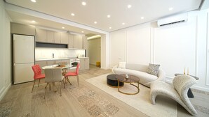 Una cocina moderna con armarios blancos, un comedor con mesa y sillas redondas, y una sala de estar con sofá y mesa de centro.