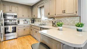 A modern kitchen with stainless steel appliances, wooden cabinets, a large island, and two potted plants. - 1 Mi to Broadway at the Beach: Home w/ Large Yard! (Myrtle Beach)