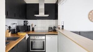 Una cocina compacta con gabinetes negros, una campana extractora de acero inoxidable, horno integrado, tostadora y cafetera.