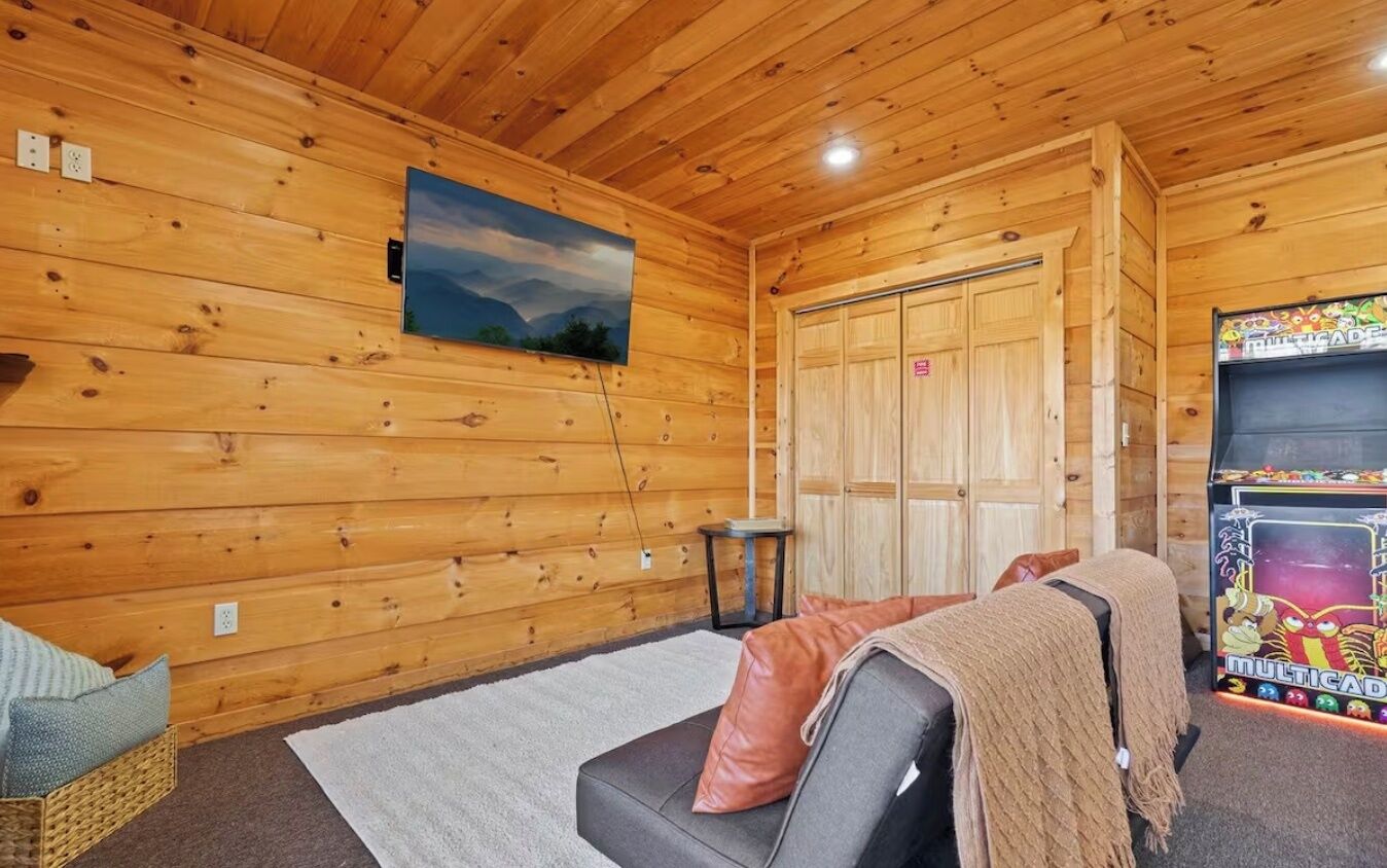 A wooden cabin interior with a sofa, a small table, a TV, and a door.
