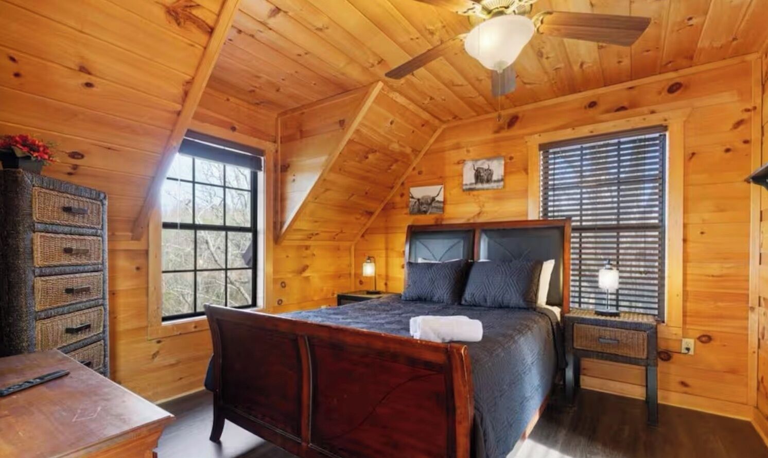 Una camera da letto accogliente in una baita di legno, con un letto grande, una cassettiera e una ventola a soffitto.