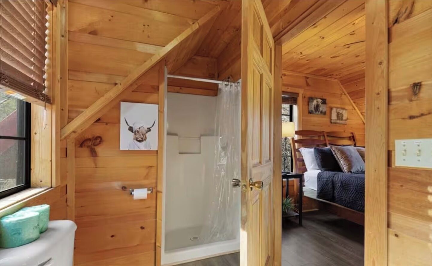 A wooden cabin interior with a shower, a bed, and a window with blinds.
