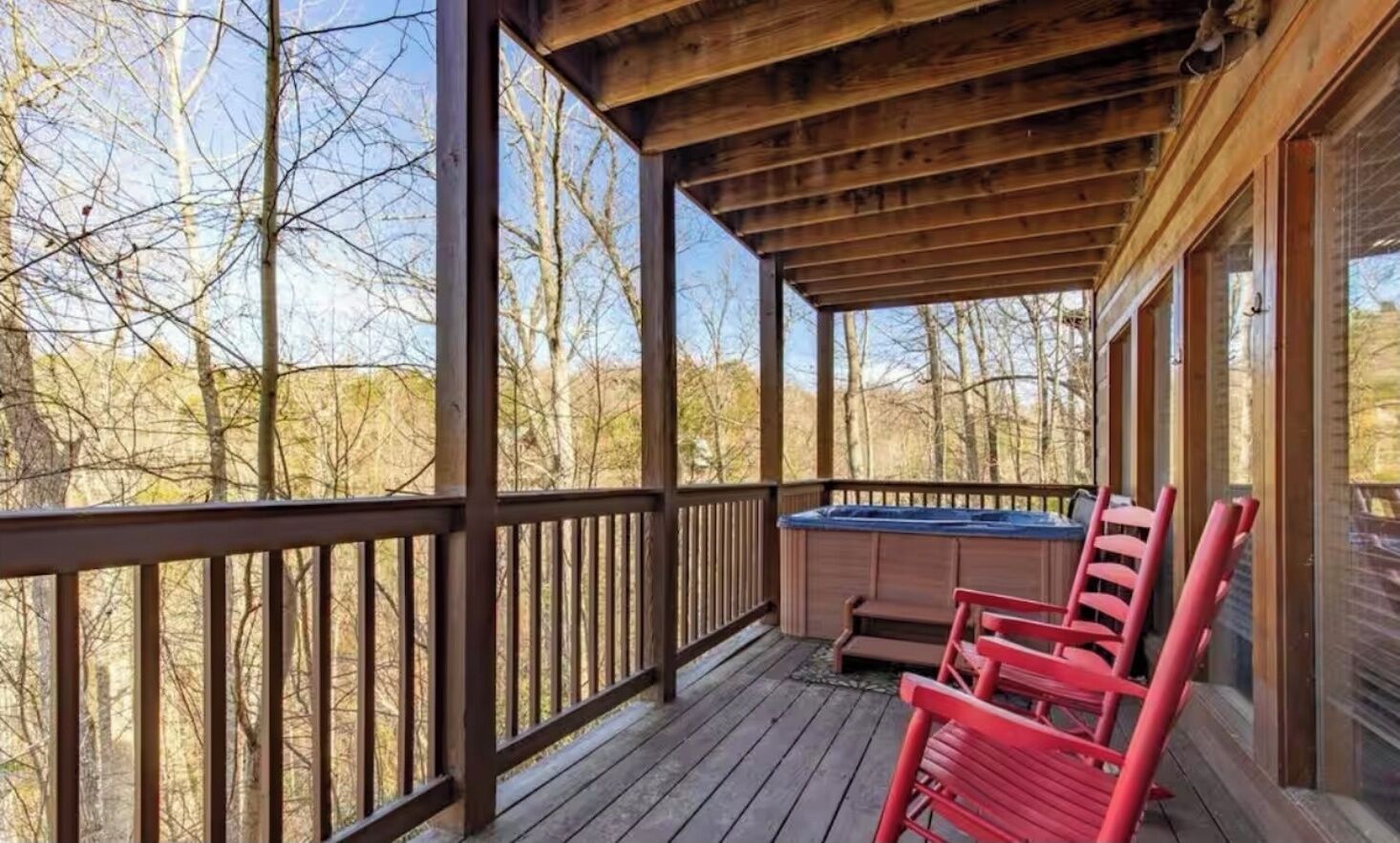 A wooden deck with a hot tub and two red chairs.
