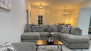 Een moderne woonkamer met een hoekbank, een salontafel en decoratieve kussens.