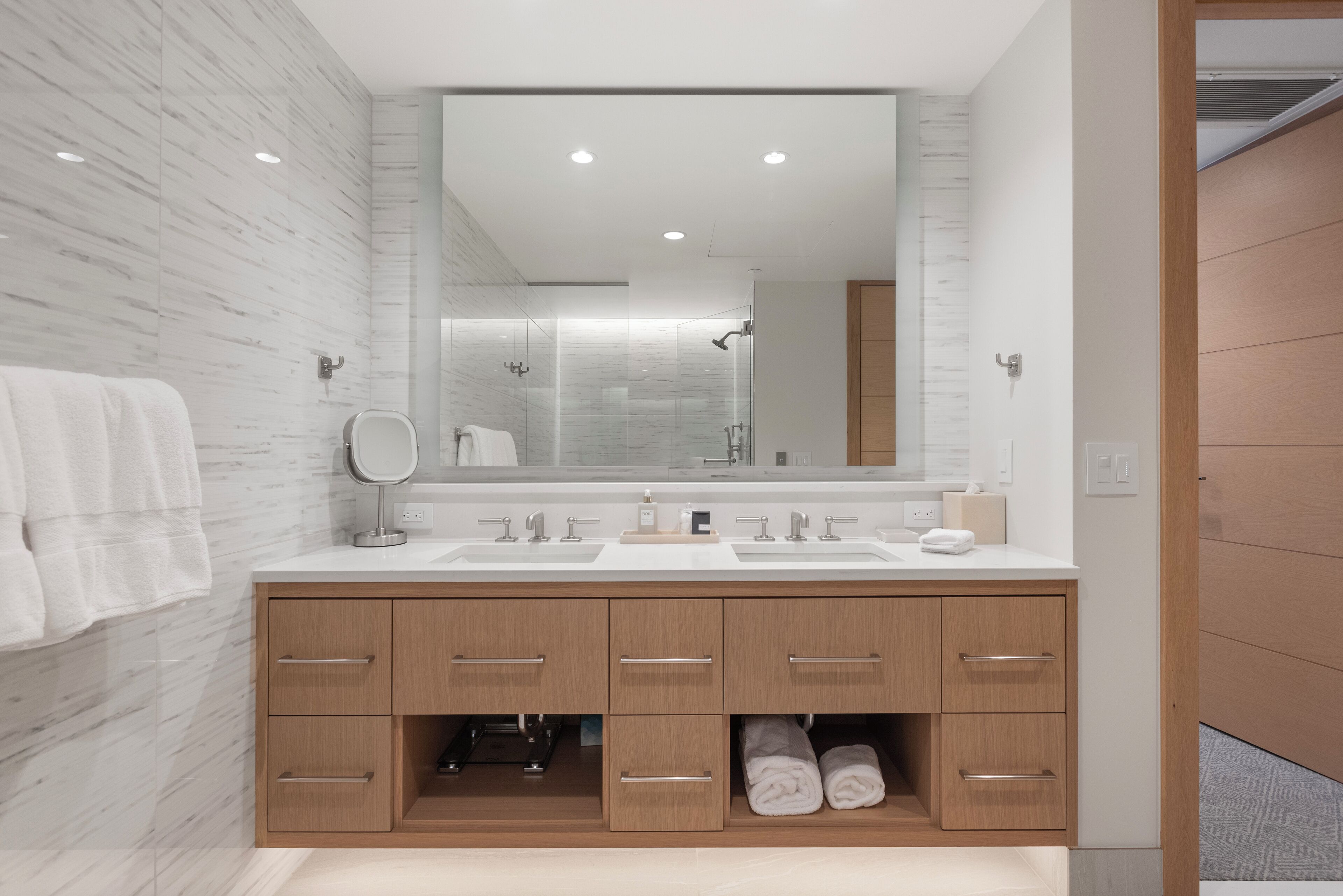 A modern bathroom with a large mirror, two sinks, and wooden cabinetry.