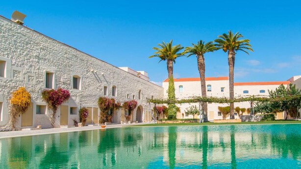 Una piscina con agua cristalina, rodeada de edificios de piedra y palmeras.