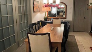 Un comedor con una mesa y sillas de madera, una lámpara colgante y una puerta con espejo.