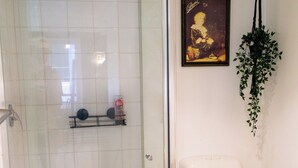 A bathroom with a glass-enclosed shower, a toilet, and a shelf with toiletries. - Cozy Melbourne Studio Digital Detox Space (Melbourne)