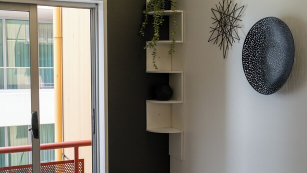 A room with a sliding glass door, a small plant on a white shelf, and two wall decorations. - Cozy Melbourne Studio Digital Detox Space (Melbourne)