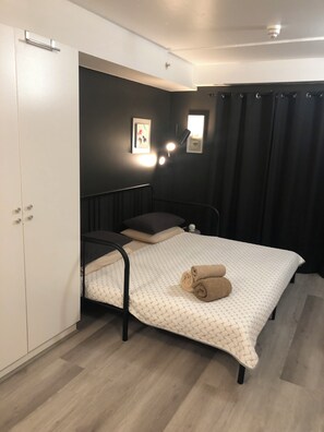 A bedroom with a bed, a wardrobe, a bedside table, and two wall-mounted lights.
