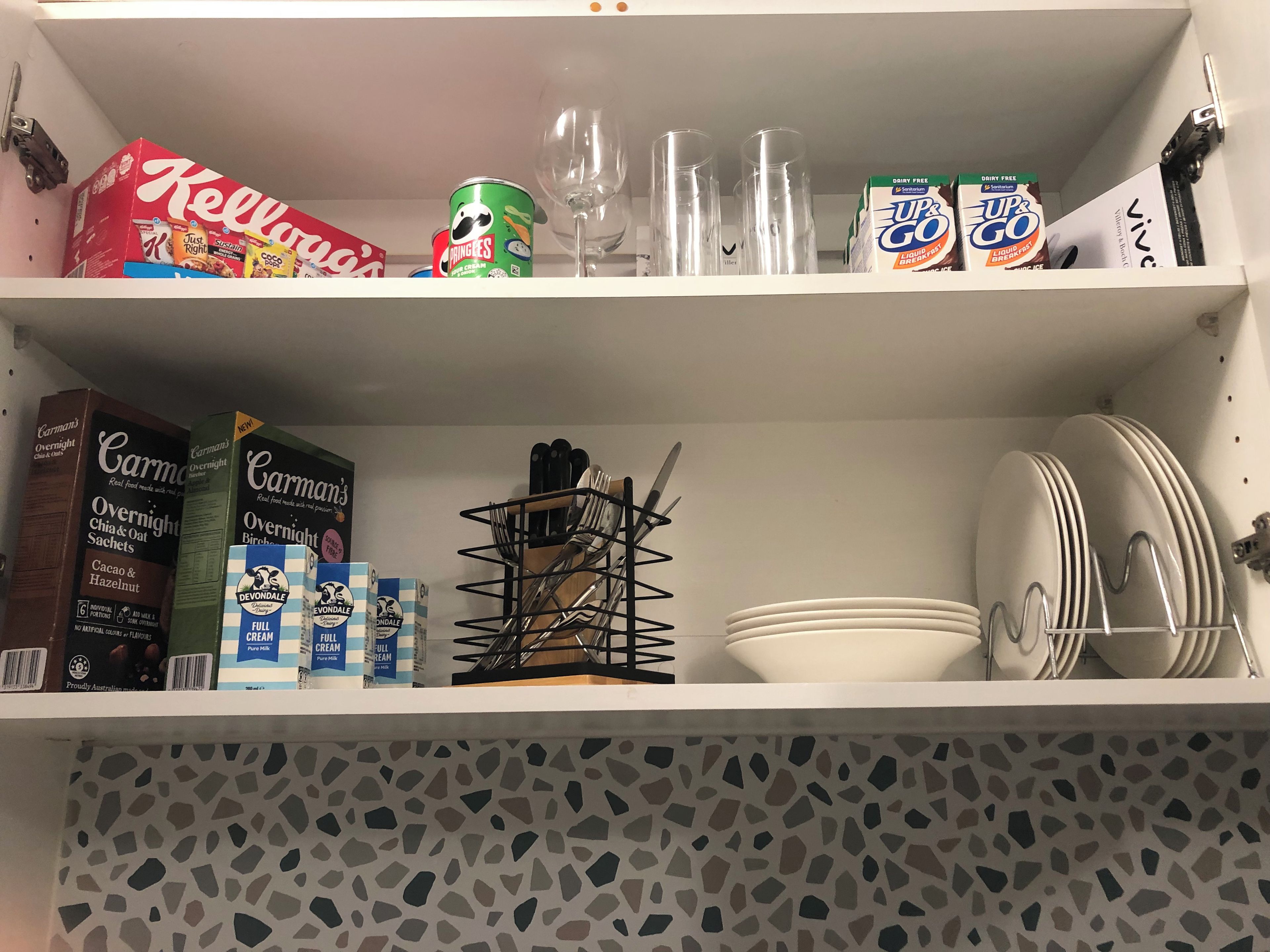 A kitchen shelf with various food items, including cereal boxes, a can of Pringles, and a box of UP&GO.
