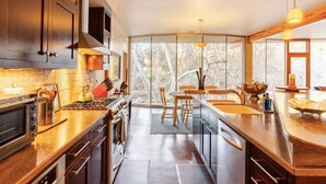 A modern kitchen with a central island, built-in appliances, and large windows offering a view of trees. - River Spirit- Arquitectural wonder of the Sequoias (Three Rivers)