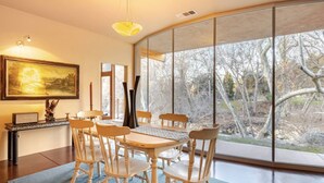 A dining area with a round table and six chairs, a painting on the wall, and a view of trees through large windows. - River Spirit- Arquitectural wonder of the Sequoias (Three Rivers)