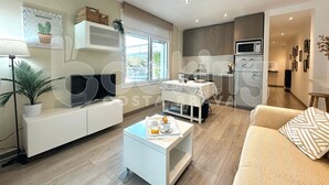 A modern living room with a sofa, coffee table, and a TV. There is a kitchen area with a microwave and a dining table.