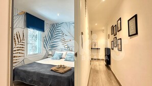 A modern bedroom with a large bed, a window with a view, and a hallway with framed pictures.