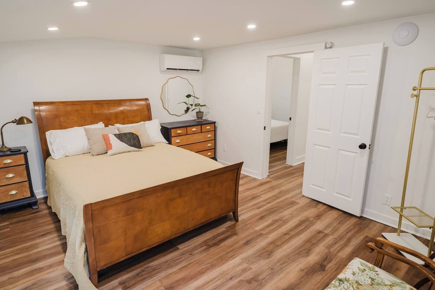 Un dormitorio con cama de madera, una mesita de noche, un tocador y una puerta que da a otra habitación.