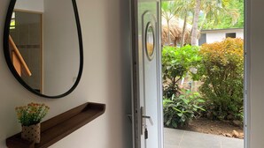 A room with a mirror, a wooden shelf with a potted plant, and a door leading to a garden with tropical plants. - Tiki Ora Lodge - HURA  (Bora Bora)