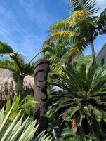 Un jardín tropical con una estructura de piedra, palmeras y un techo de paja.