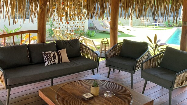 A covered outdoor seating area with a wooden ceiling, a hanging chandelier, and a view of a pool. - Tiki Ora Lodge - HURA  (Bora Bora)