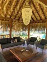 Un área de estar al aire libre techada, con techo de madera, un candelabro colgante y vista a una piscina.