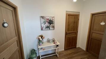 Un couloir avec des portes en bois, une petite table ornée d’objets décoratifs et un tableau floral accroché au mur.