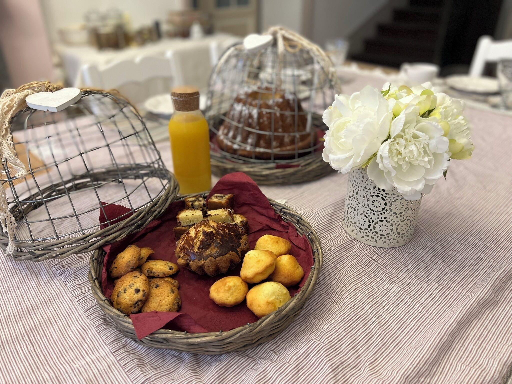 A table with baskets of baked goods, a bottle of juice, and a vase of flowers.