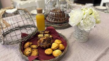 A table with baskets of baked goods, a bottle of juice, and a vase of flowers.
